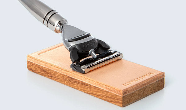 A close-up of a Gillette Fusion 5-blade shaver resting on a rectangular shaped leather razor sharpener.